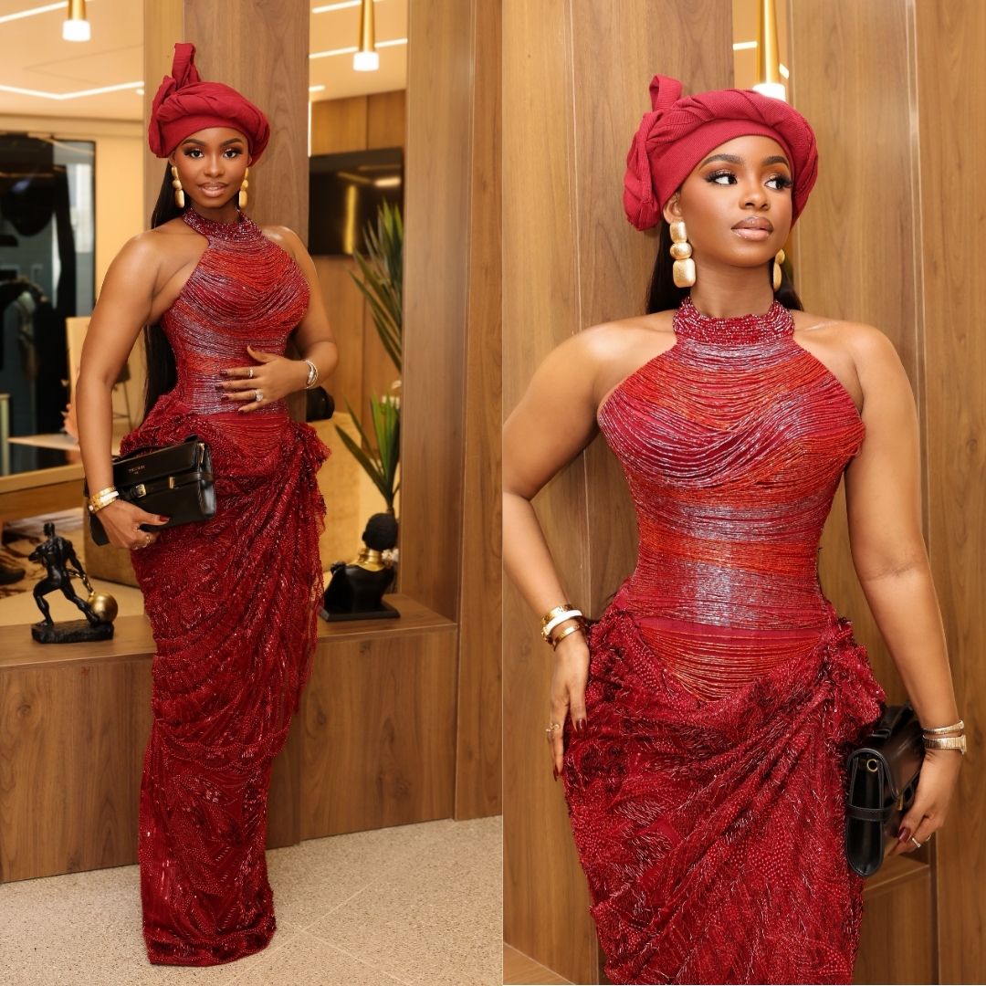 Priscilla Ojo in a high-neck halter fashion gown with crimson beaded linework, draped hip accents, matching turban gele, and gold statement earrings.