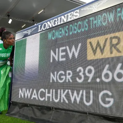 Goodness Nwachukwu posing beside the Longines scoreboard displaying her 39.66m F42 discus world record at Glasgow 2026.