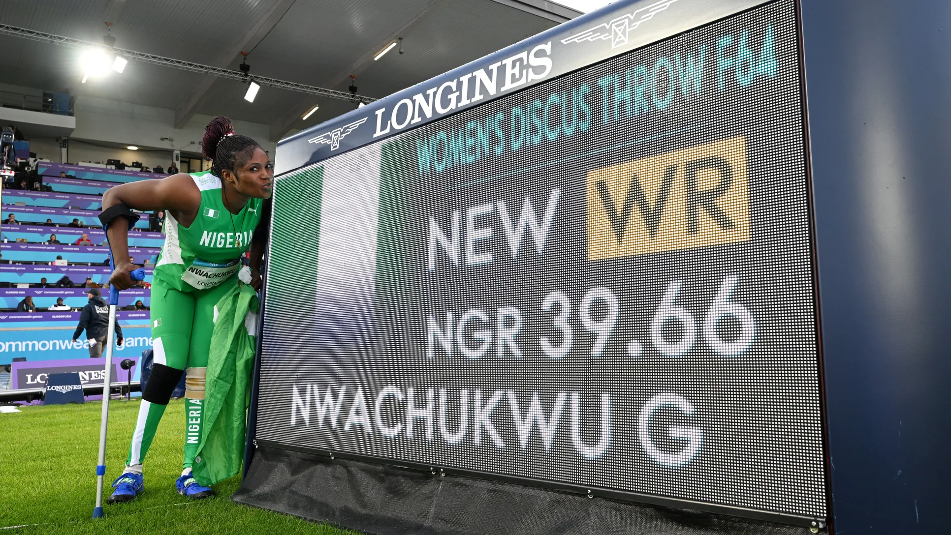 Goodness Nwachukwu posing beside the Longines scoreboard displaying her 39.66m F42 discus world record at Glasgow 2026.