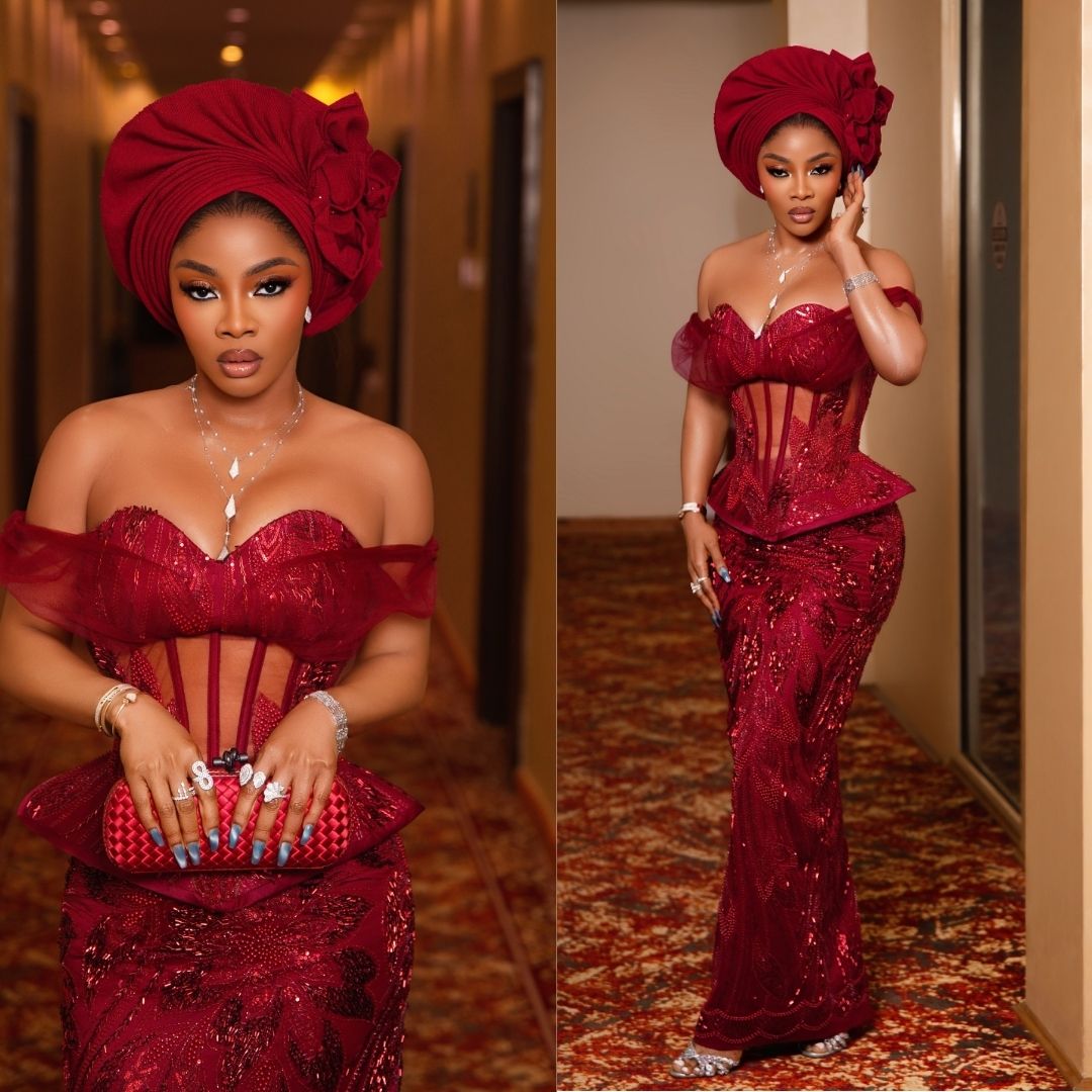 Toke Makinwa in an off-the-shoulder crimson sequined lace corset gown with exposed boning, peplum waist, rosette-detailed gele, and woven red clutch.