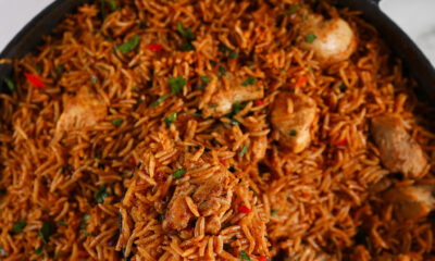 A spoon scoops up a serving of fluffy basmati rice and marinated chicken pieces from a large pot.