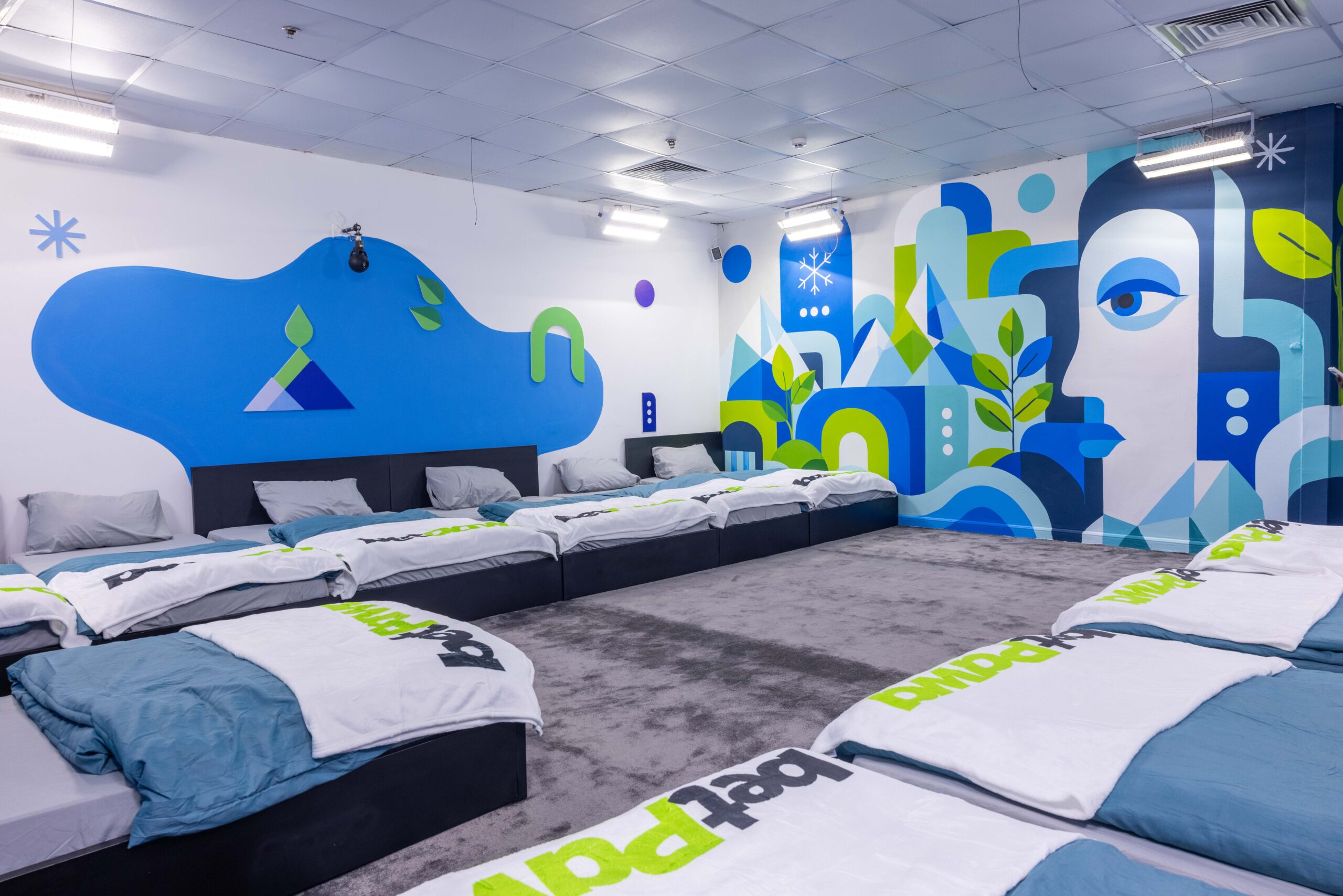 Housemates' bedroom in the Big Brother Naija Season 11 house featuring blue bed sheets, grey pillows, and a blue abstract face mural