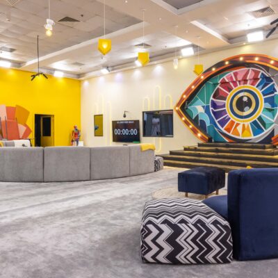 Main lounge in the Big Brother Naija Season 11 house featuring a large colourful illuminated Big Brother eye stage setup and digital countdown clock on