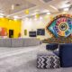 Main lounge in the Big Brother Naija Season 11 house featuring a large colourful illuminated Big Brother eye stage setup and digital countdown clock on