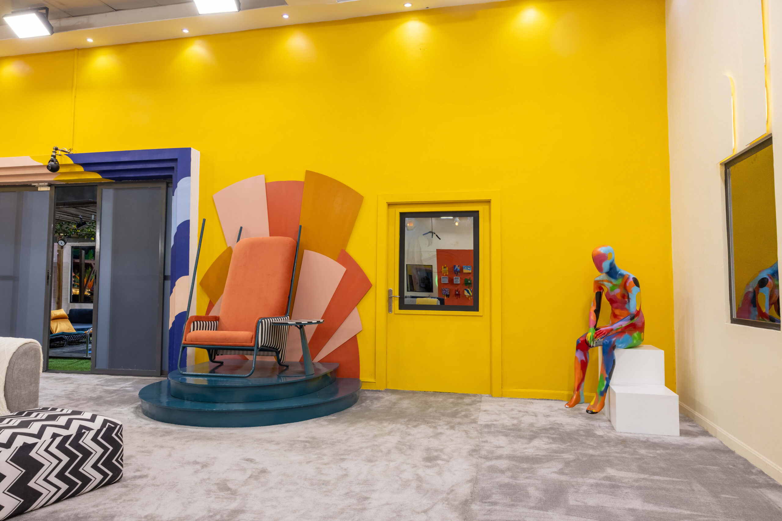 Bright yellow lounge wall in the Big Brother Naija Season 11 house with an orange high-back statement chair and artistic mannequin