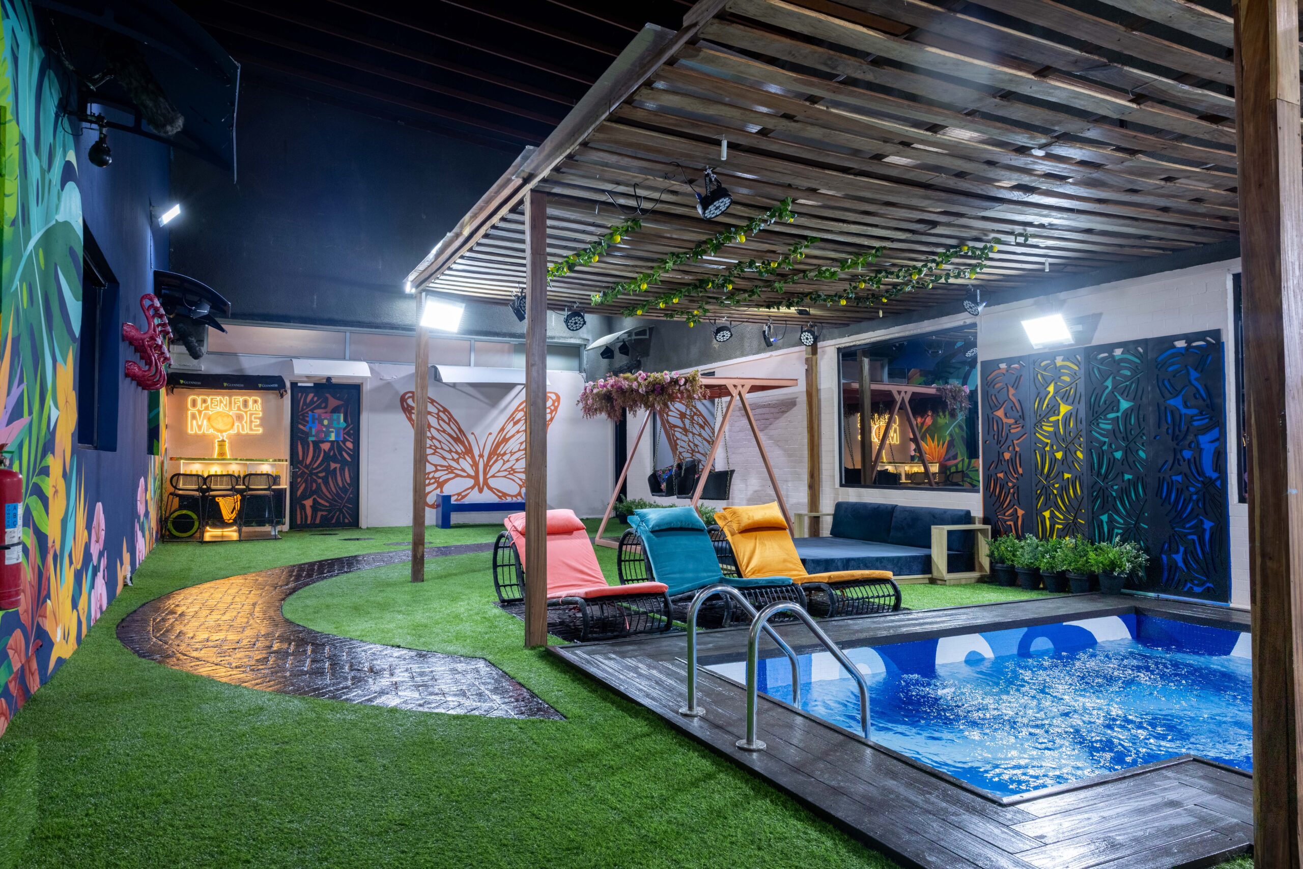Outdoor garden swimming pool area in the Big Brother Naija Season 11 house with colorful sun loungers and a wooden pergola