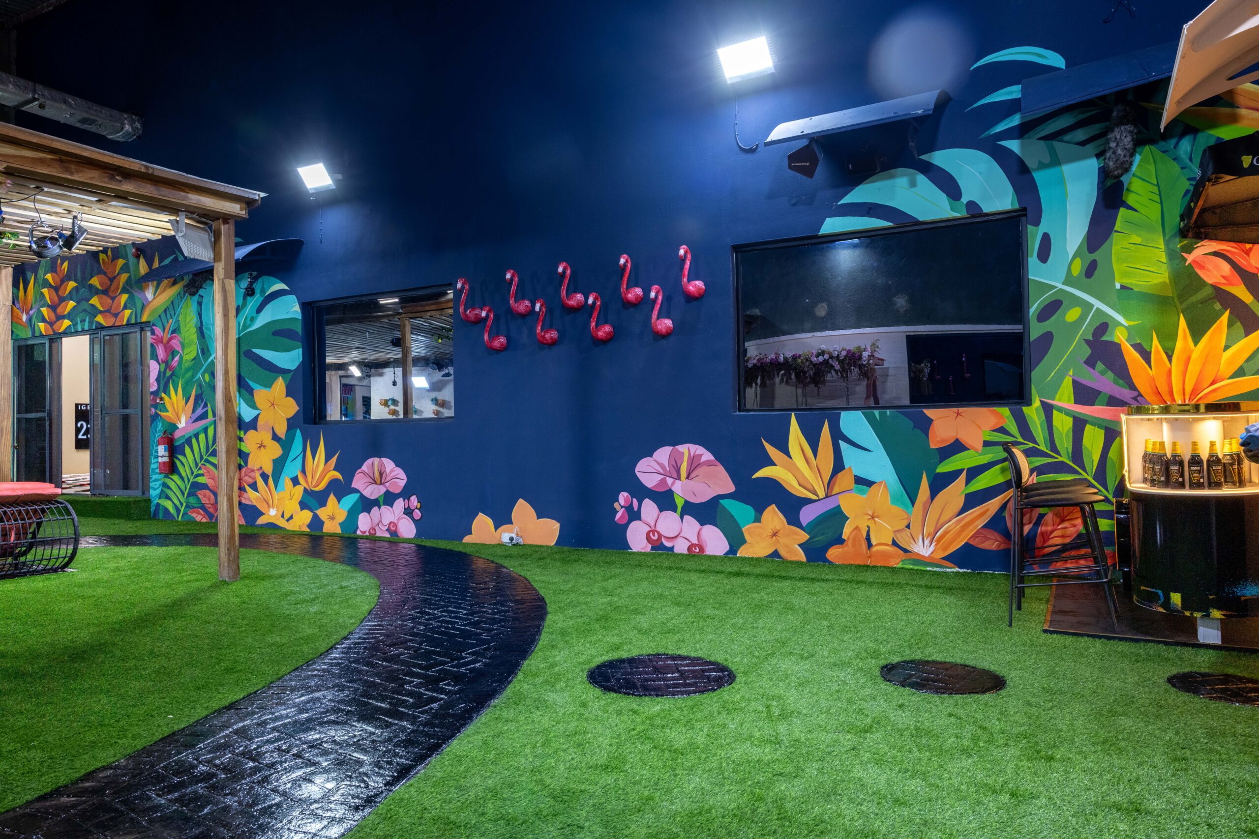 Navy blue garden wall in the Big Brother Naija Season 11 outdoor courtyard with bright tropical floral murals and red flamingo accents