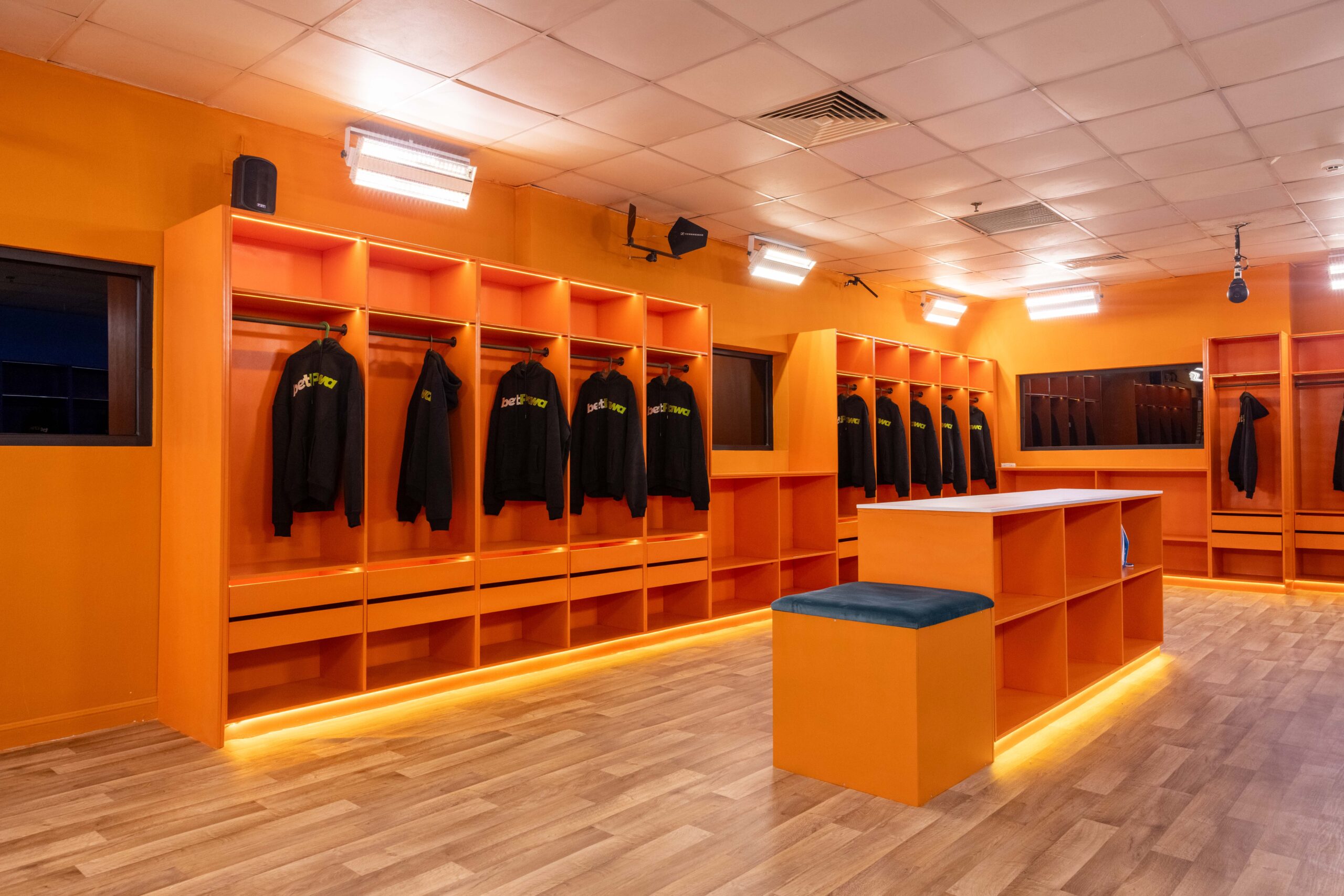 Bright orange dressing room in the Big Brother Naija Season 11 house with custom open storage lockers and central island seating