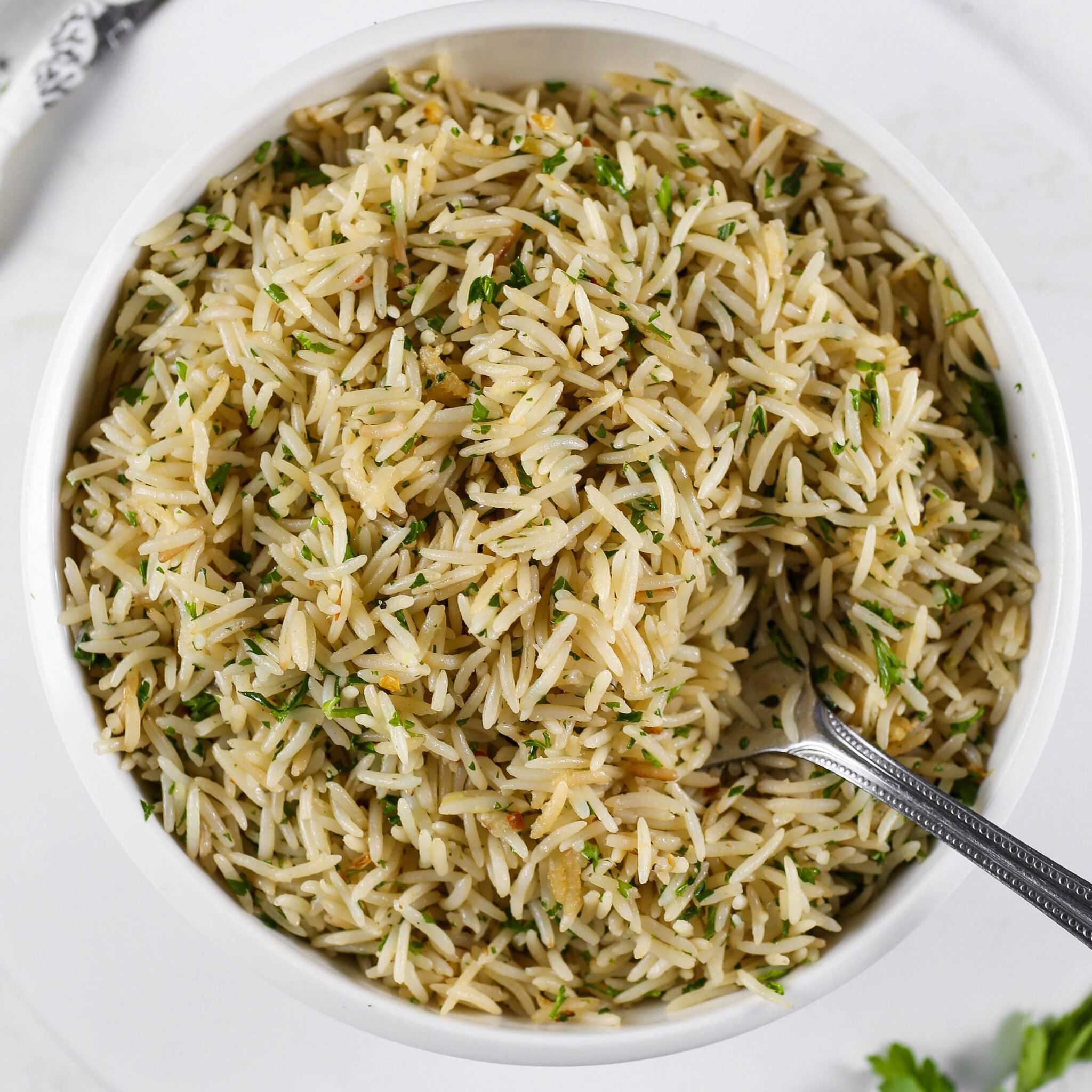 Kikifoodies garlic herb basmati rice garnished with chopped fresh parsley in a white bowl with a spoon.