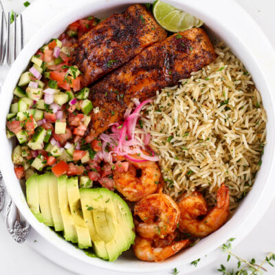 Kikifoodies garlic herb rice served in a bowl with pan-seared salmon, grilled shrimp, sliced avocado, pickled onions, and cucumber tomato salad.