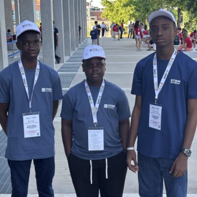 Don Anele Munachimso Marvelous, Egejurum Onyedikachi Ethan, and Chimdiebube Onwubiko wearing blue STEM Olympiad shirts and white caps outside Università Campus Bio-Medico di Roma.