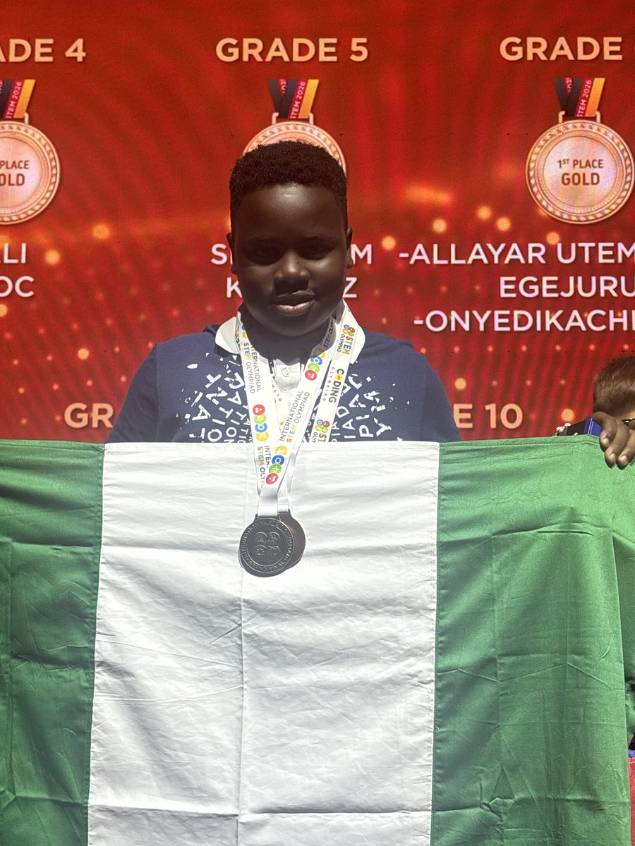 Eleven-year-old Egejurum Onyedikachi Ethan holding the Nigerian flag on stage in front of the Grade 5 world champion scoreboard.