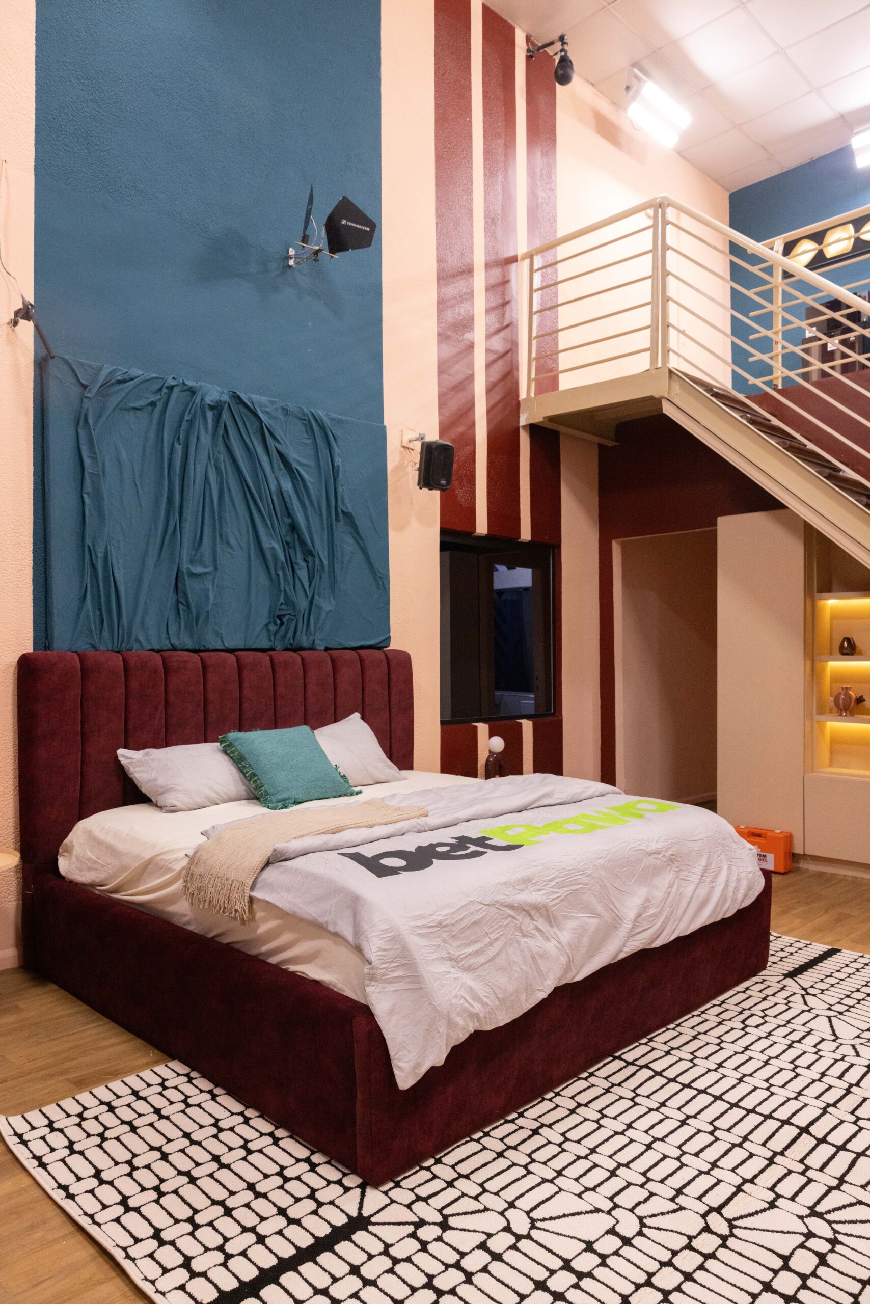 Luxury Head of House loft bedroom in the Big Brother Naija Season 11 house with a plush maroon bed and wooden mezzanine staircase