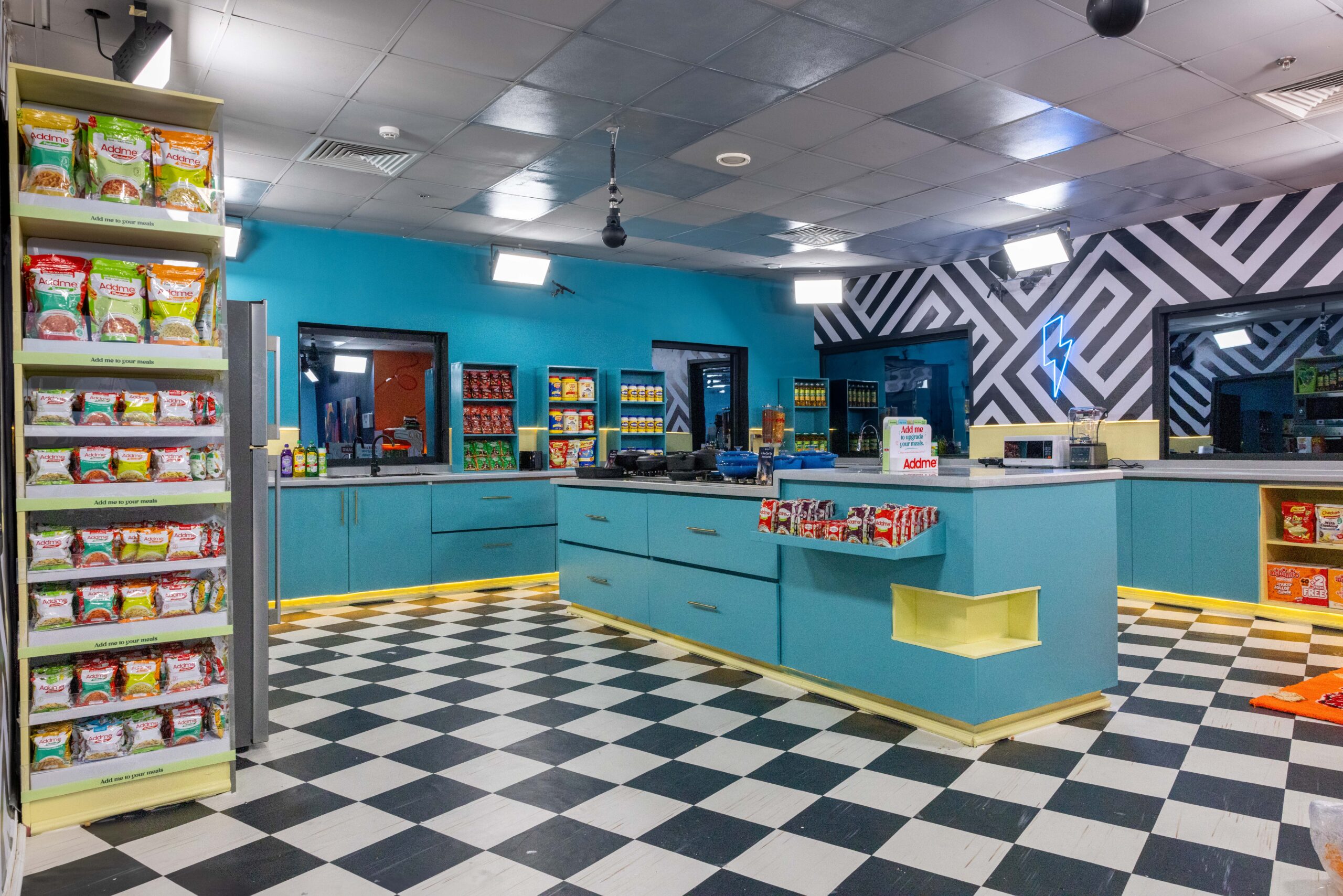 Modern teal kitchen in the Big Brother Naija Season 11 house with black and white monochrome checkered flooring and stocked pantry shelves