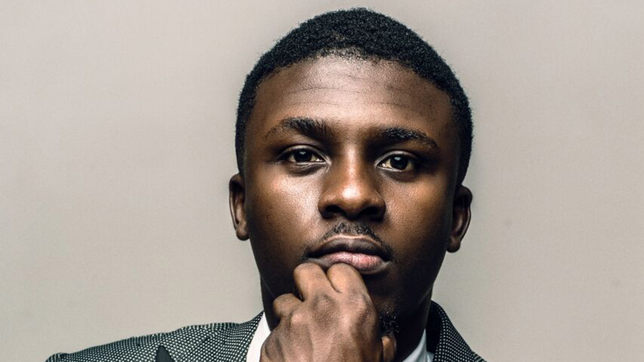 BBNaija alumnus Lolu Shomuyiwa wearing a patterned blazer and white shirt with his hand on his chin.