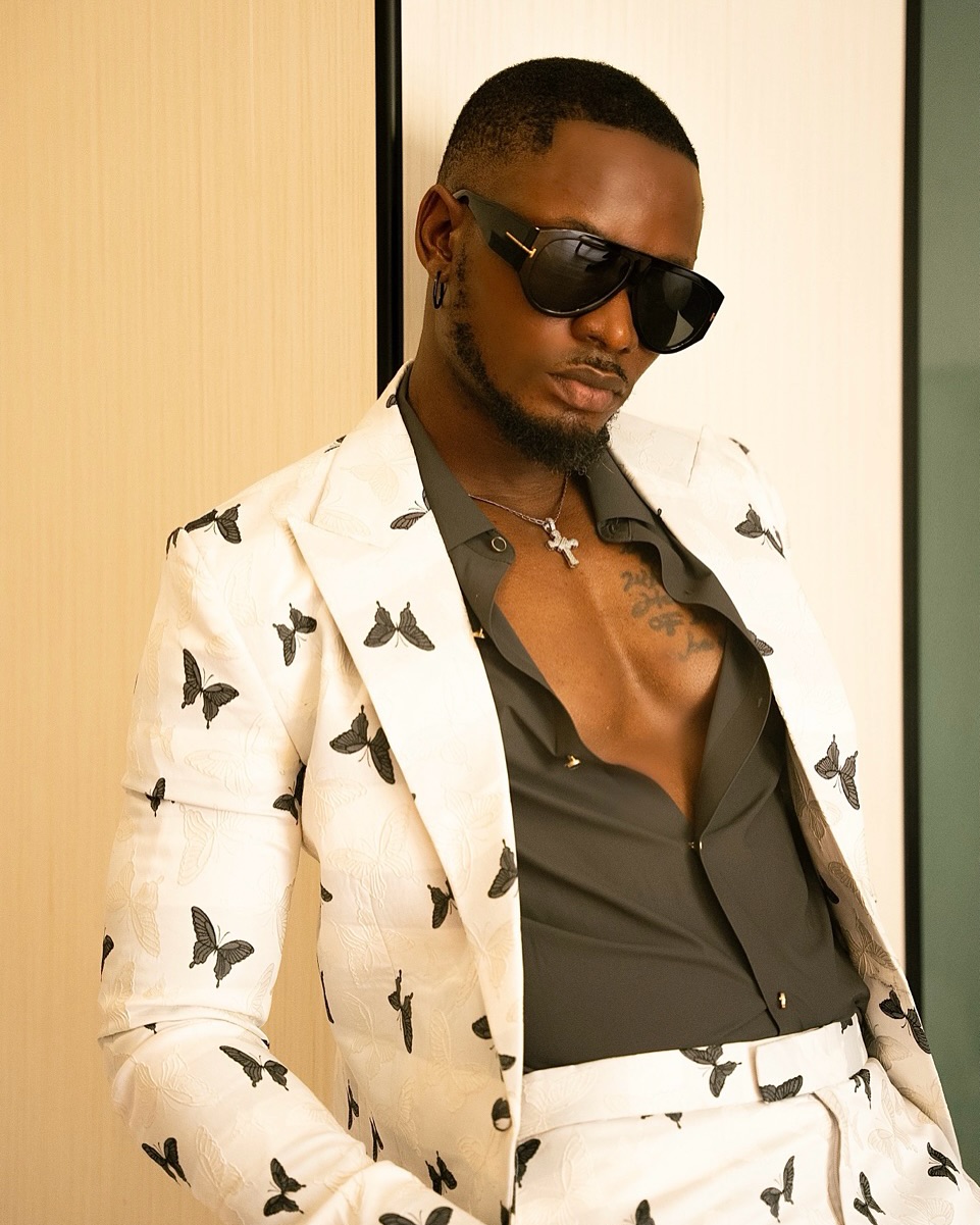 Big Brother Naija Season 9 winner Kellyrae (Kingsley Sule) wearing a white butterfly-pattern suit and black sunglasses.