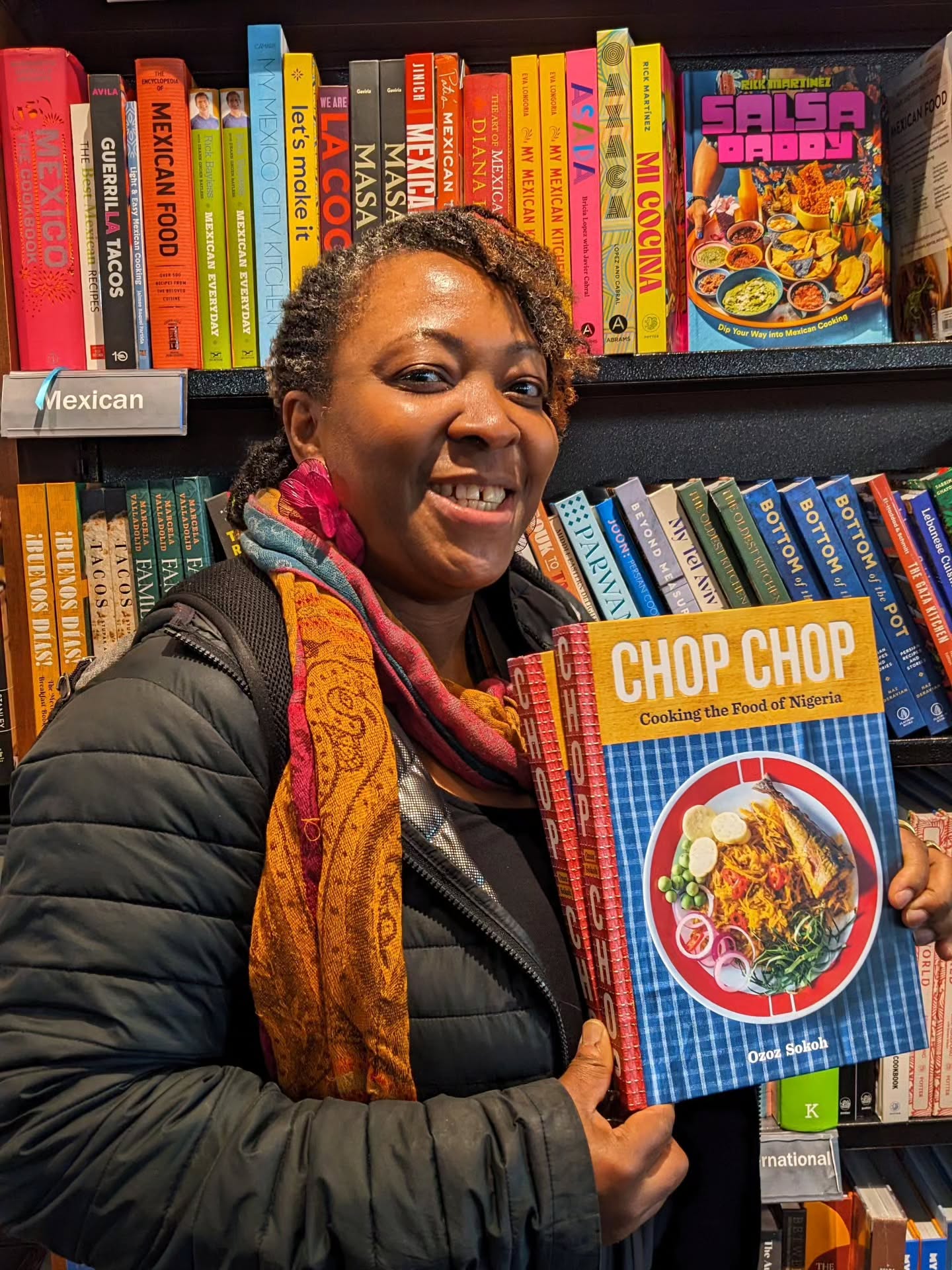 Ozoz Sokoh smiling while holding copies of her debut cookbook, Chop Chop: Cooking the Food of Nigeria, in front of a bookstore display during her New York tour in May 2025.