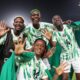 Nigeria's Super Falcons players, including Rasheedat Ajibade and Asisat Oshoala, smiling and celebrating on the pitch.