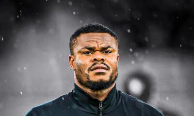 Nigerian national team goalkeeper Stanley Nwabali holding his hand over his heart in a Super Eagles walkout jacket, symbolising his commitment as he rejoins his club career.
