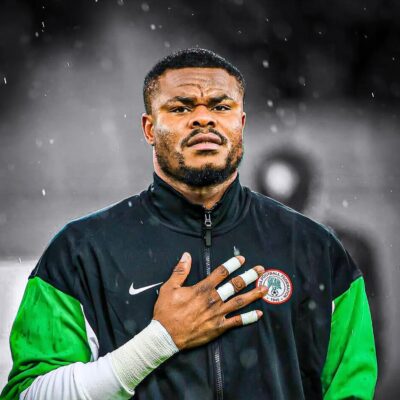Nigerian national team goalkeeper Stanley Nwabali holding his hand over his heart in a Super Eagles walkout jacket, symbolising his commitment as he rejoins his club career.