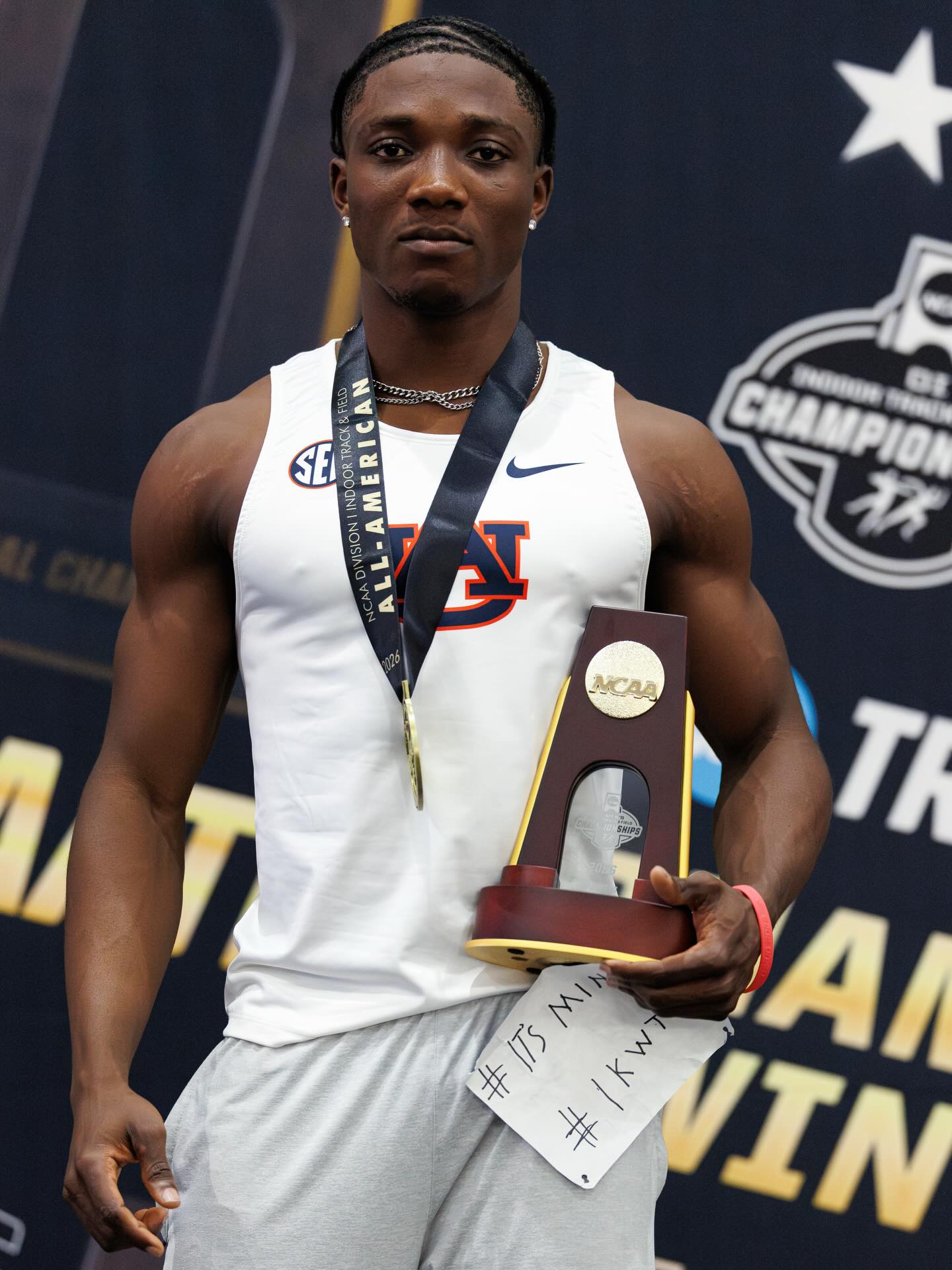 Kanyinsola Ajayi wearing his All-American medal and holding the NCAA championship trophy after running a 9.72-second 100m victory.