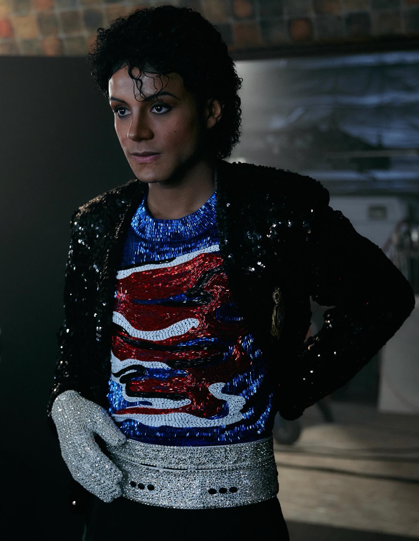 Jaafar Jackson as Michael Jackson in a black sequined military jacket over a blue, red, and silver beaded shirt with a silver sequined belt and a single rhinestone-covered glove.