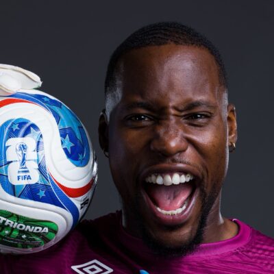DR Congo goalkeeper Lionnel Mpasi shouting in celebration while holding the official FIFA World Cup 2026 match ball on his shoulder.
