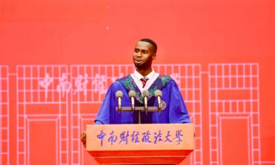 Nnabuike Chisom speaking into microphones at a wooden lectern with Chinese characters at Zhongnan University.
