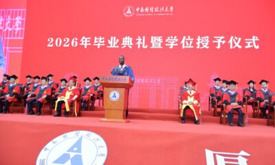 Nnabuike Chisom delivers his keynote address at a wooden podium on stage before a panel of university faculty members.