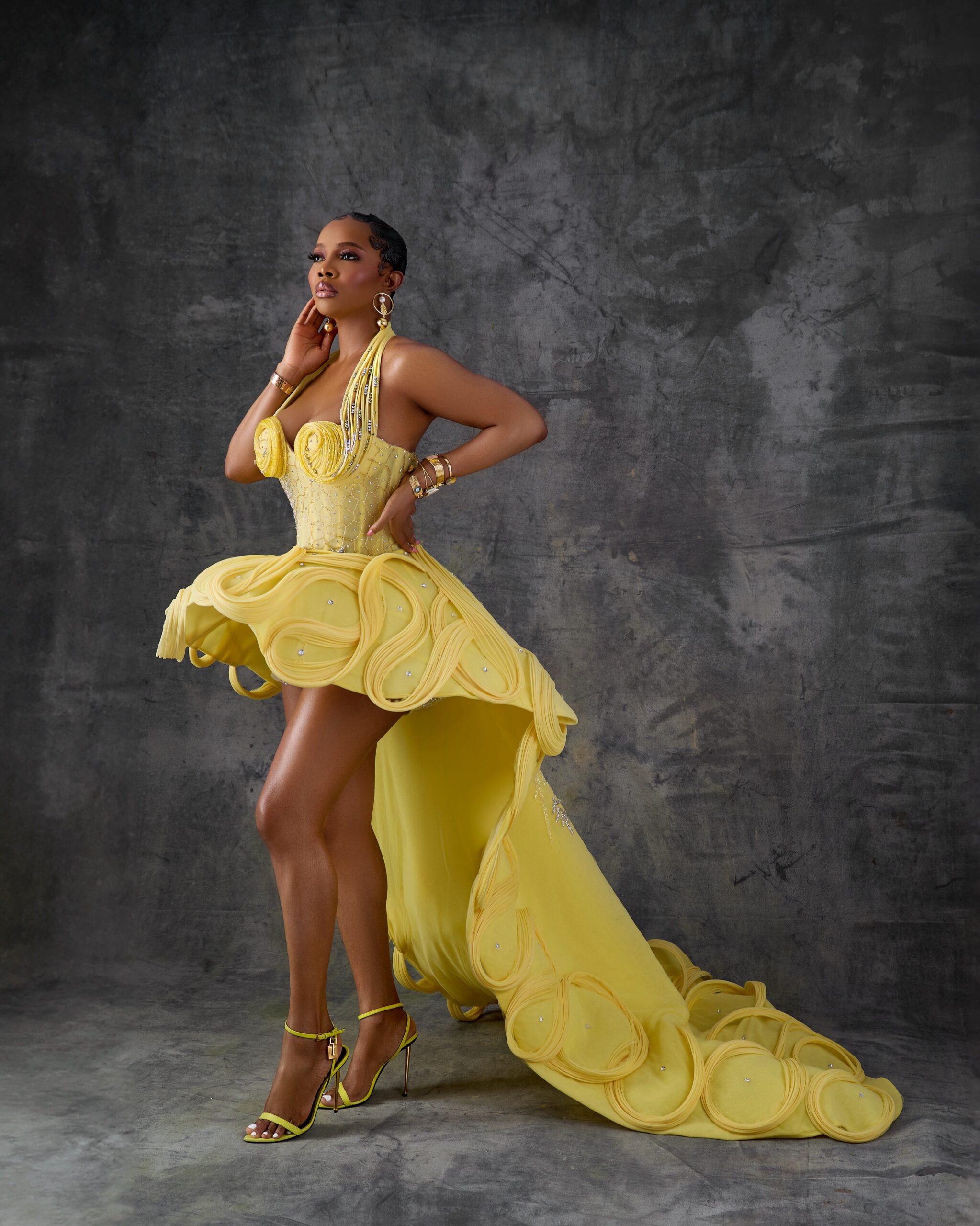 Toke Makinwa posing in a canary yellow high-low gown with fabric rosette cups and a multi-layered bubble loop skirt train by Emagine By Bukola.