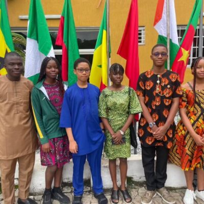 Six Team Nigeria secondary school student representatives dressed in traditional African attire standing in front of continental flags at the Pan-African Mathematics Olympiad in Yamoussoukro Ivory Coast.