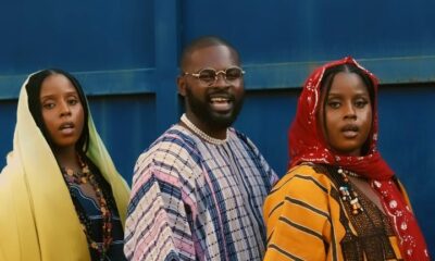 Falz wearing a striped dashiki alongside musical duo Oiza x Meyi in traditional Northern attire standing behind jerrycans in the Na Je music video.