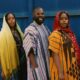 Falz wearing a striped dashiki alongside musical duo Oiza x Meyi in traditional Northern attire standing behind jerrycans in the Na Je music video.