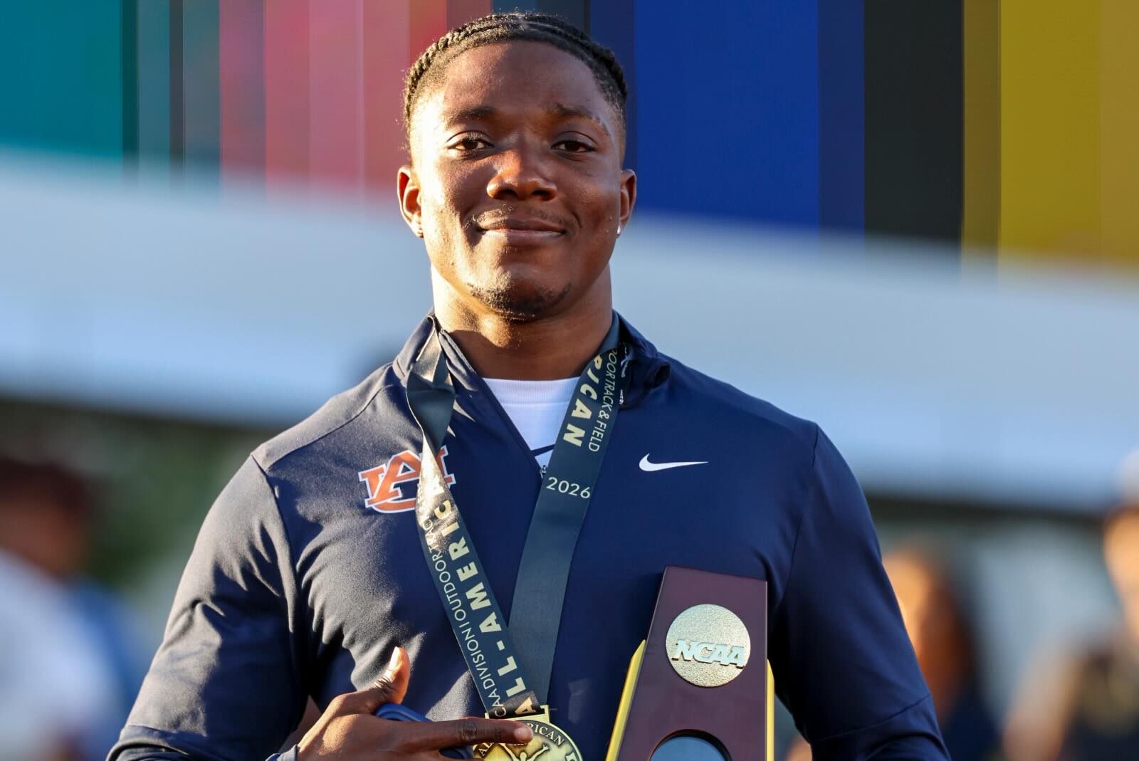 Kanyinsola Ajayi in Auburn track uniform holding his NCAA Indoor Championship trophy after equalling the collegiate 60m record of 6.45 seconds.