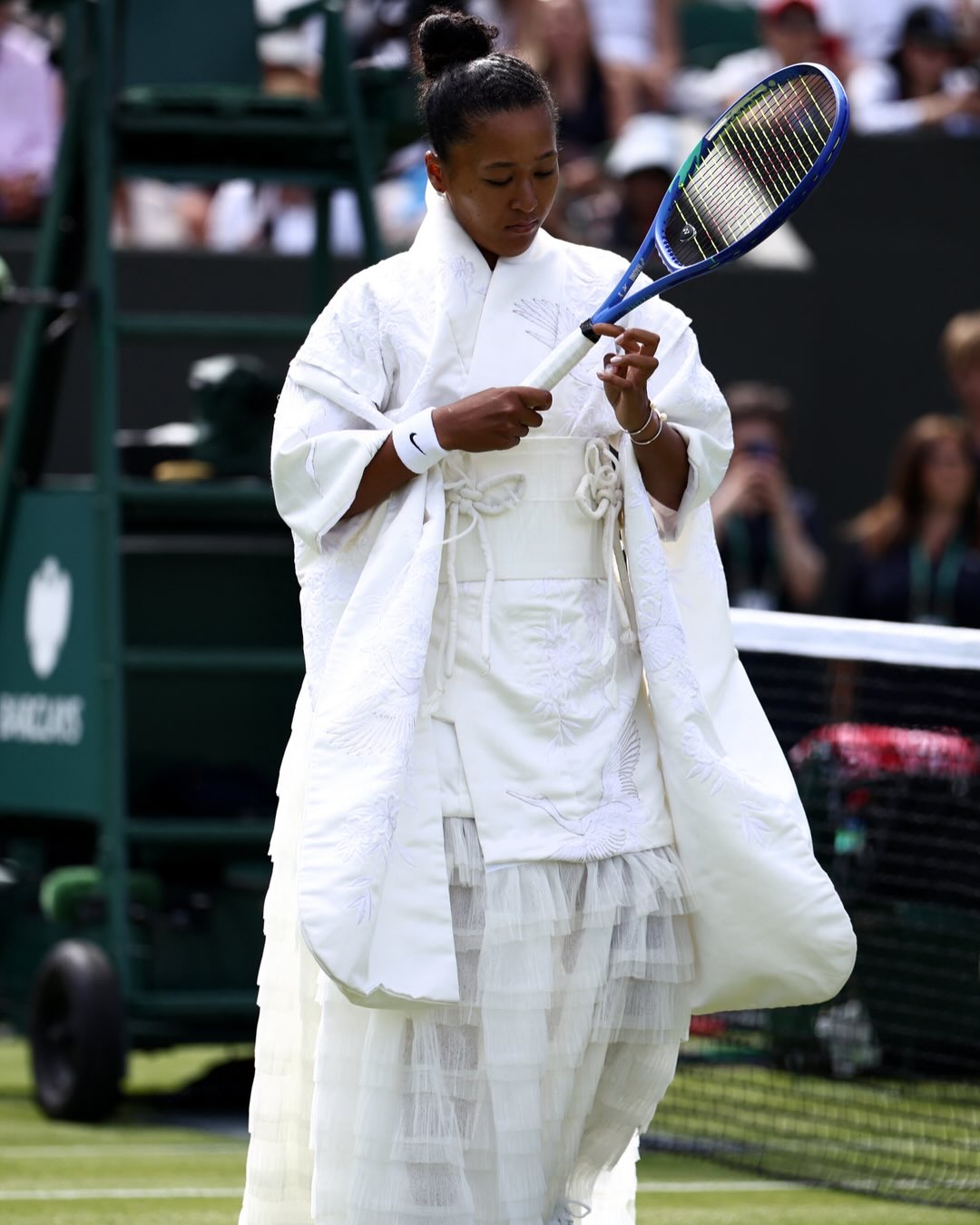 Naomi Osaka holding a tennis racket on court at Wimbledon while wearing a custom white upcycled kimono gown.