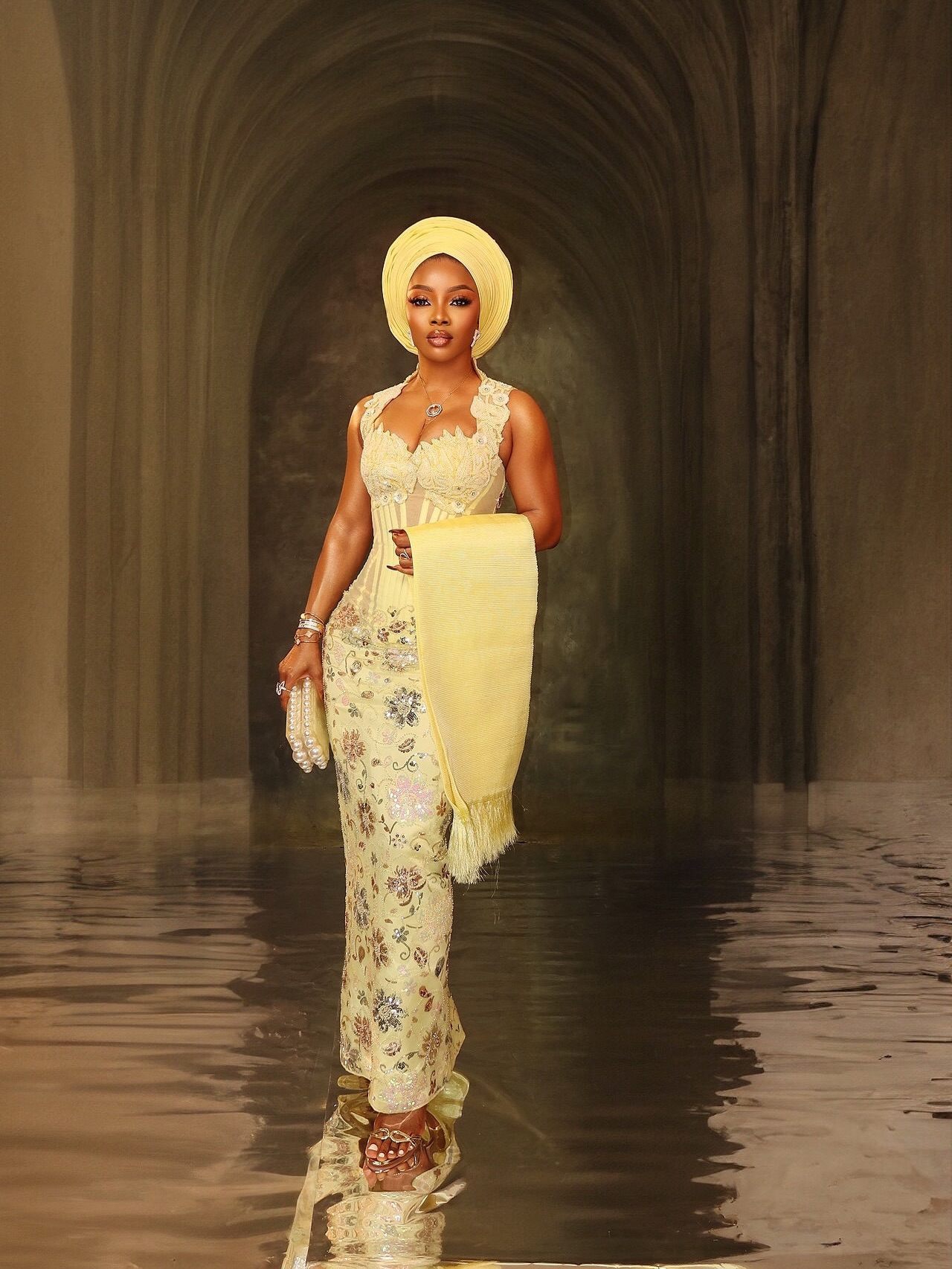 Toke Makinwa posing in a pale yellow sequined lace column skirt, matching structured corset bodice, yellow traditional Gele headtie, and ipele by Fiolakemi Atelier.