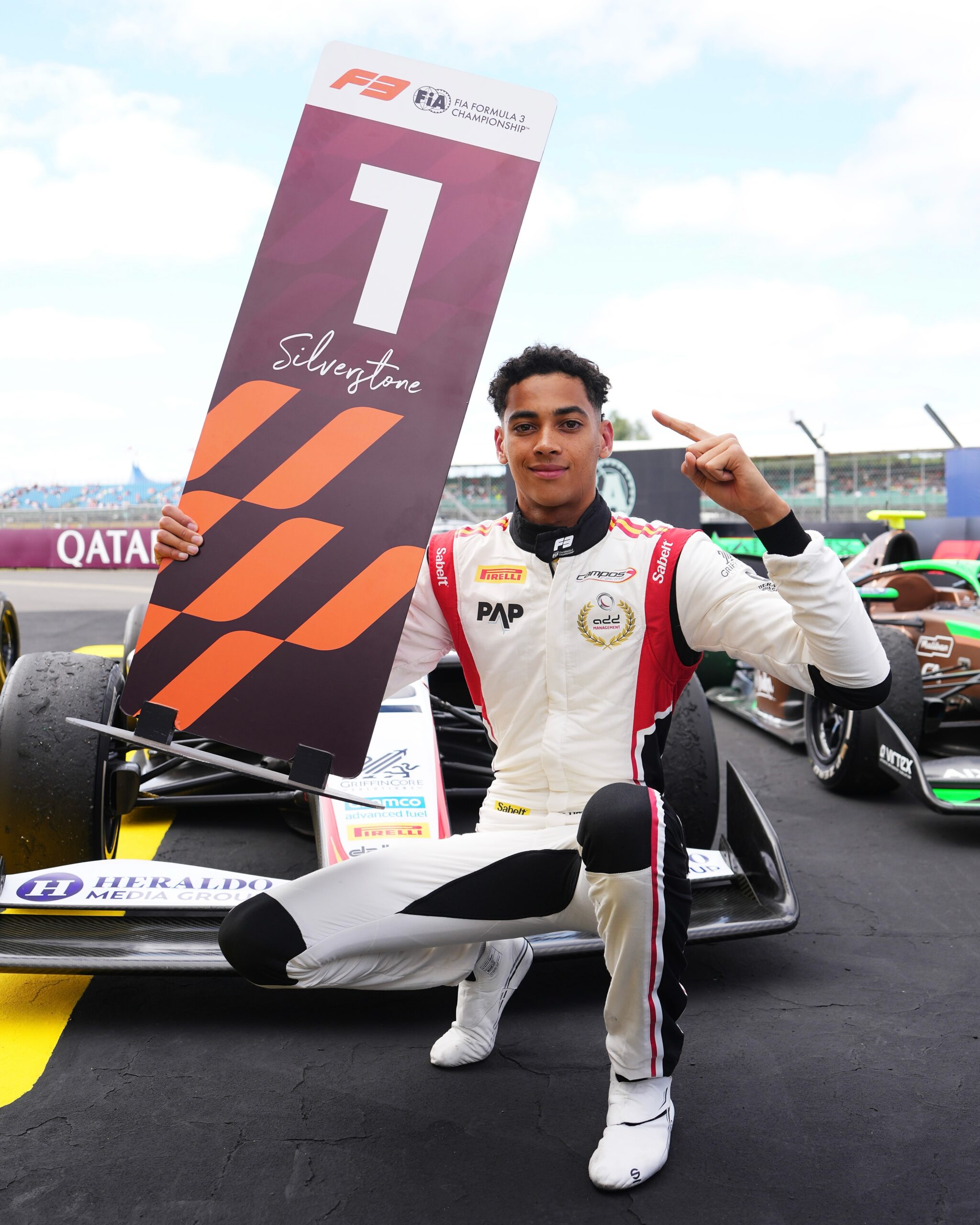 Ugo Ugochukwu crouching on the track track holding a number one Silverstone victory board after the Formula 3 race.