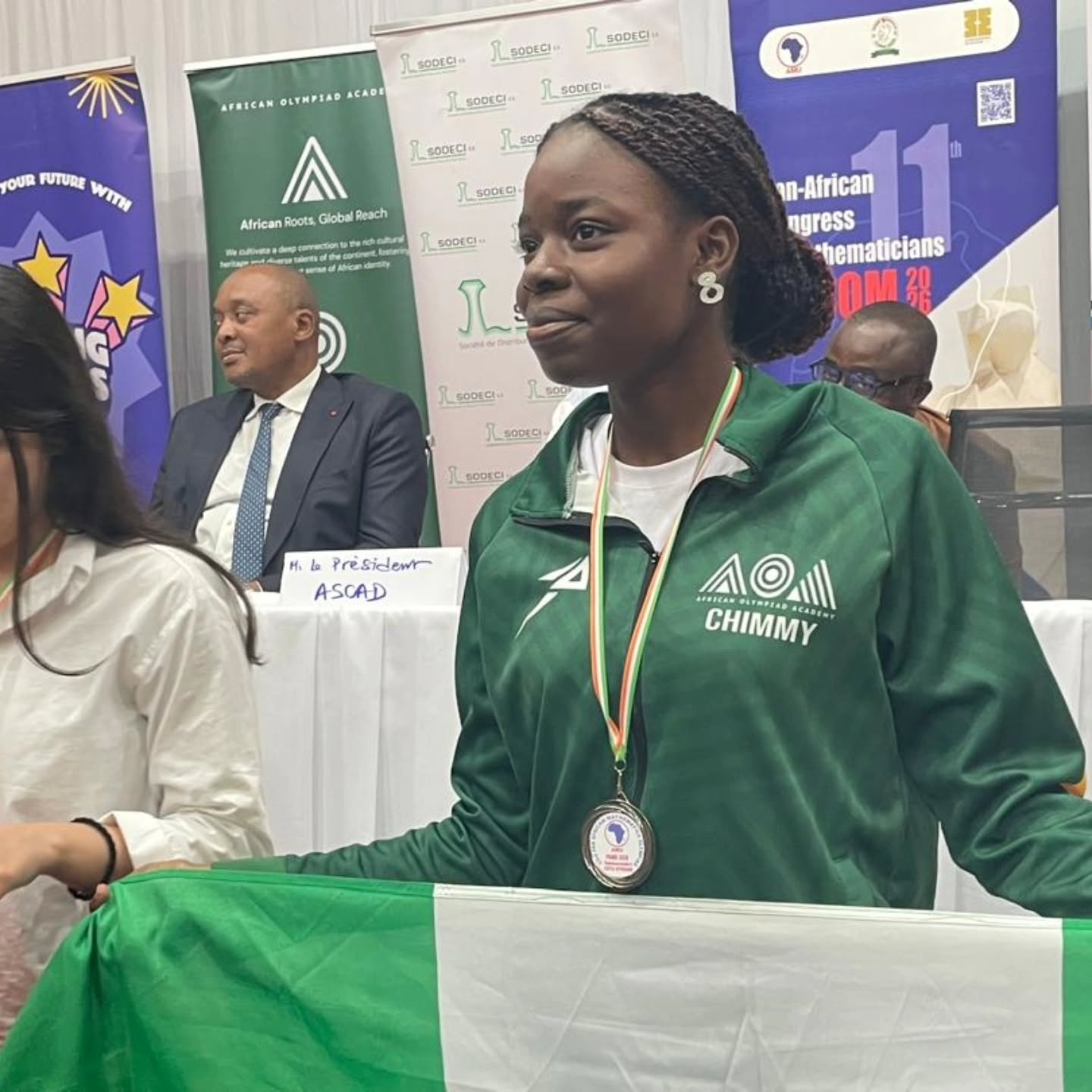 Nigerian student Chimfumnanya Aghaduno wearing a green Team Nigeria jacket and a silver medal while holding the national flag at the Pan-African Mathematics Olympiad awards ceremony.