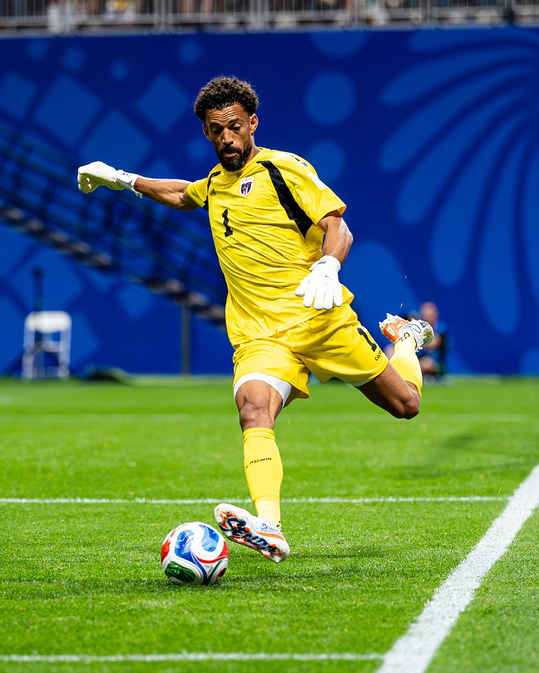 Goalkeeper Vozinha kicking the tournament match ball downfield from the penalty box in his yellow uniform.