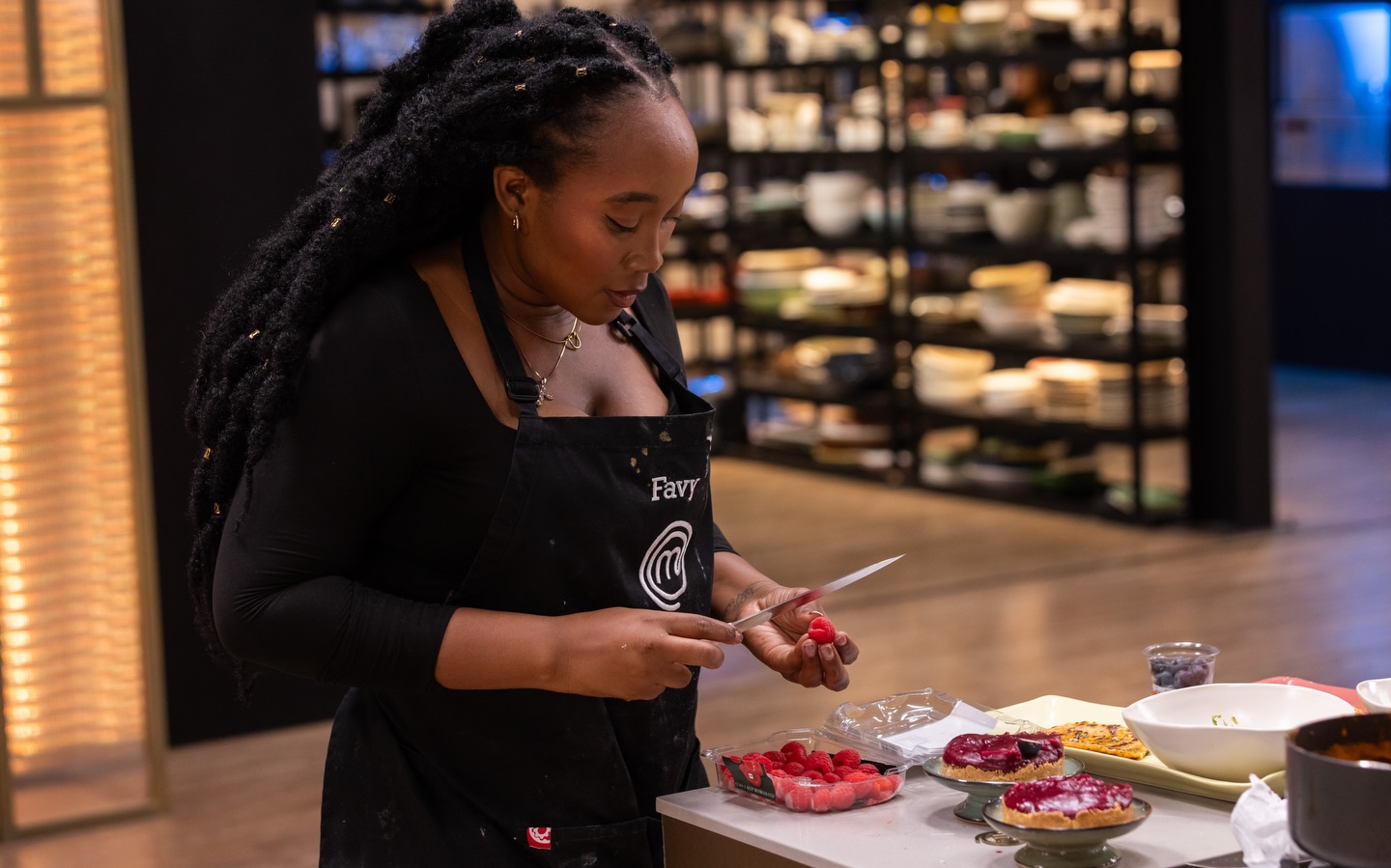 MasterChef Nigeria contestant Favy Bessan carefully plating raspberries for a dessert course during a cooking challenge.