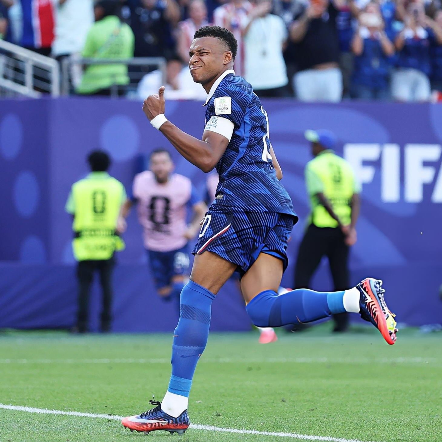 France captain Kylian Mbappé running down the pitch and gesturing a thumbs-up celebration after scoring a goal at the 2026 FIFA World Cup.