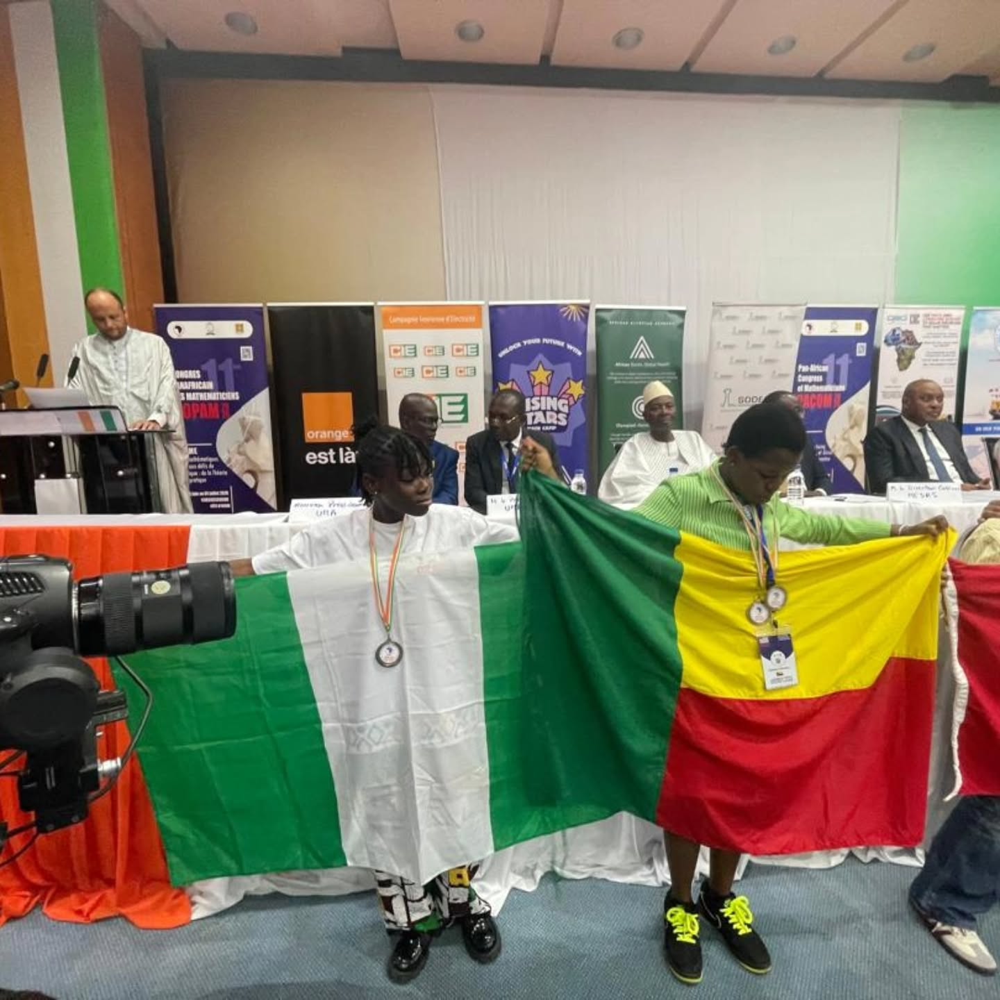 A Nigerian female student wearing a silver medal holds the Nigerian national flag on the podium at the 2026 Pan-African Mathematics Olympiad alongside a representative from Mali.