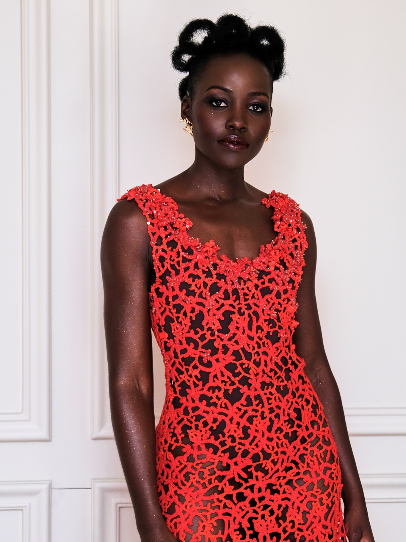 Lupita Nyong'o in a coral-red open-work lace Chanel dress, with architectural natural hair loops and smoky eye makeup by Nick Barose.
