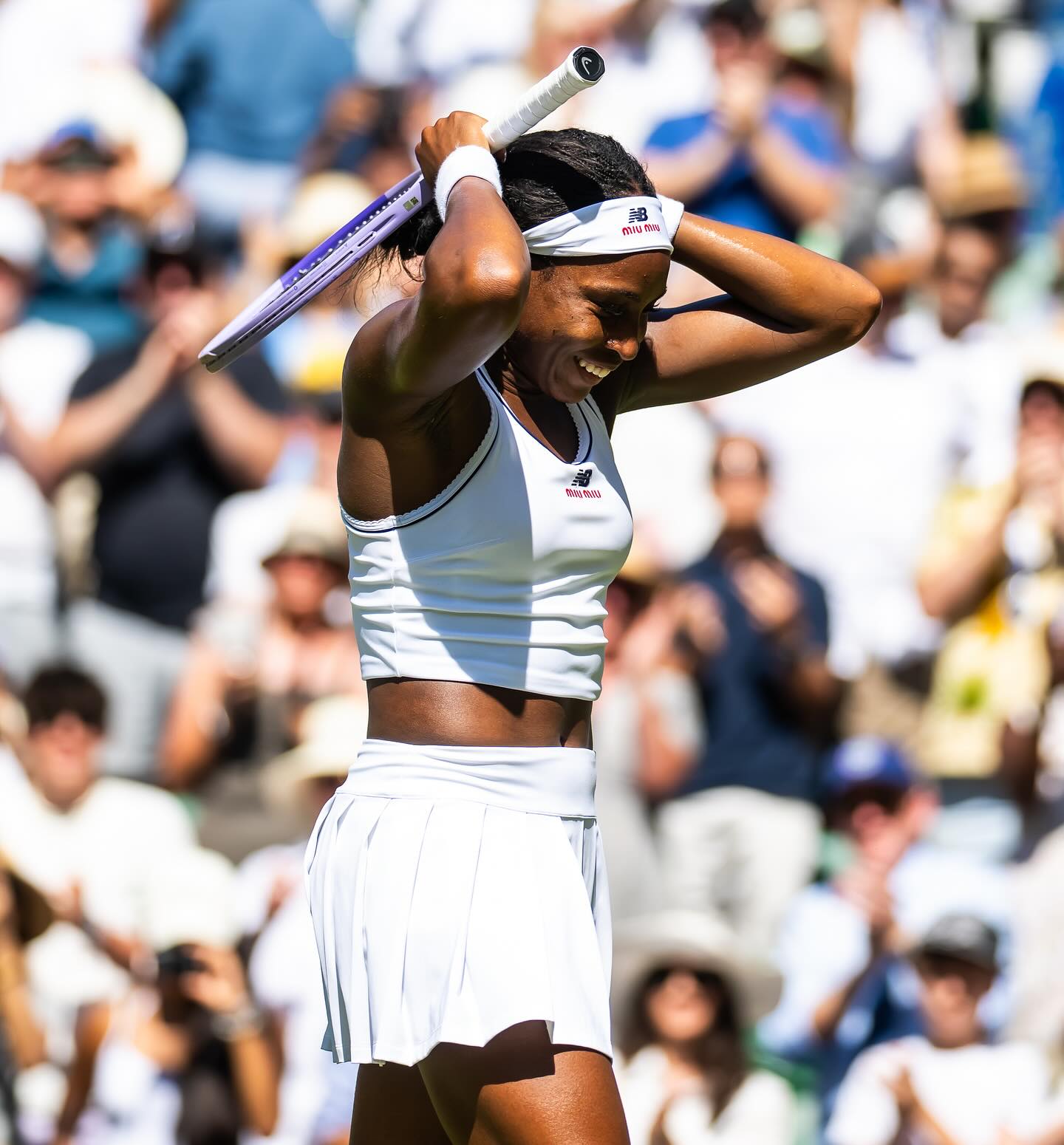 Coco Gauff smiling with pure relief and holding her tennis racket behind her head after winning her match at Wimbledon.