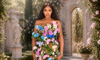 Idia Aisien standing in a stone courtyard wearing a strapless flesh-toned gown adorned with trailing green vines and multi-coloured roses.