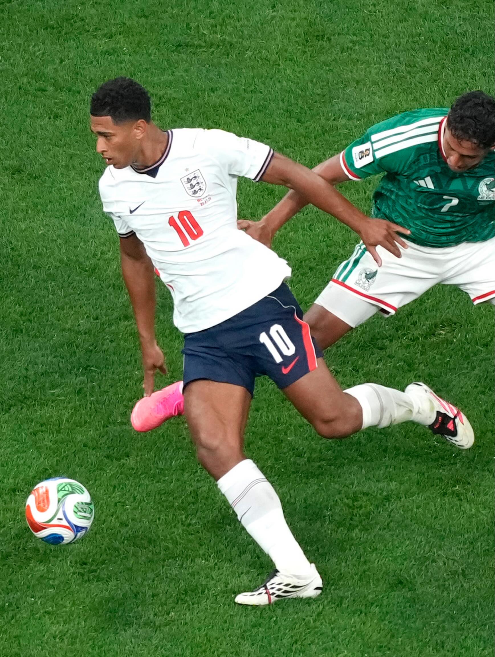 Jude Bellingham of Jamaican descent wearing the white number 10 England shirt while dribbling a football past a Mexico player in a green kit on the pitch.