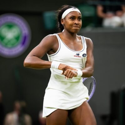 Coco Gauff smiling and hitting her signature "clock it" victory gesture on Centre Court after winning her Wimbledon quarter-final.