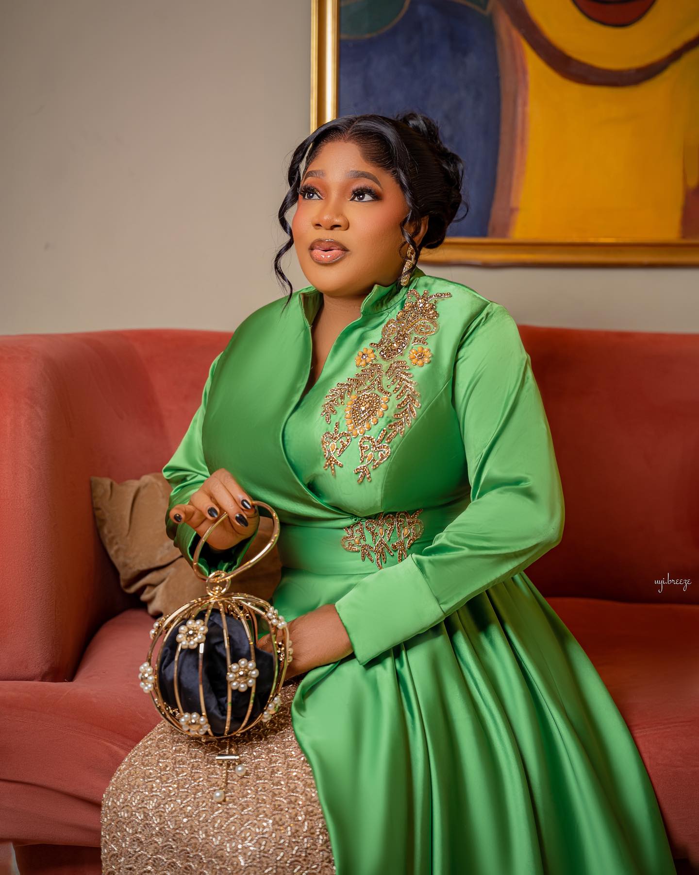 Toyin Abraham Ajeyemi wearing a structured apple-green satin wrapped jacket blouse with gold embroidery on the shoulder and waist, holding a spherical pearl-embellished handbag.