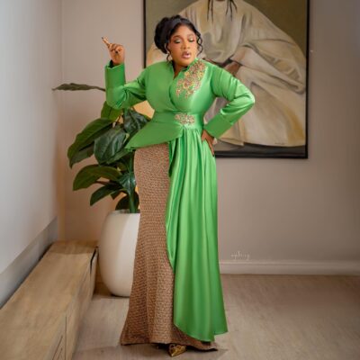 Toyin Abraham Ajeyemi with a fluid apple-green satin panel cascading from the waist over a fitted floor-length gold column skirt.