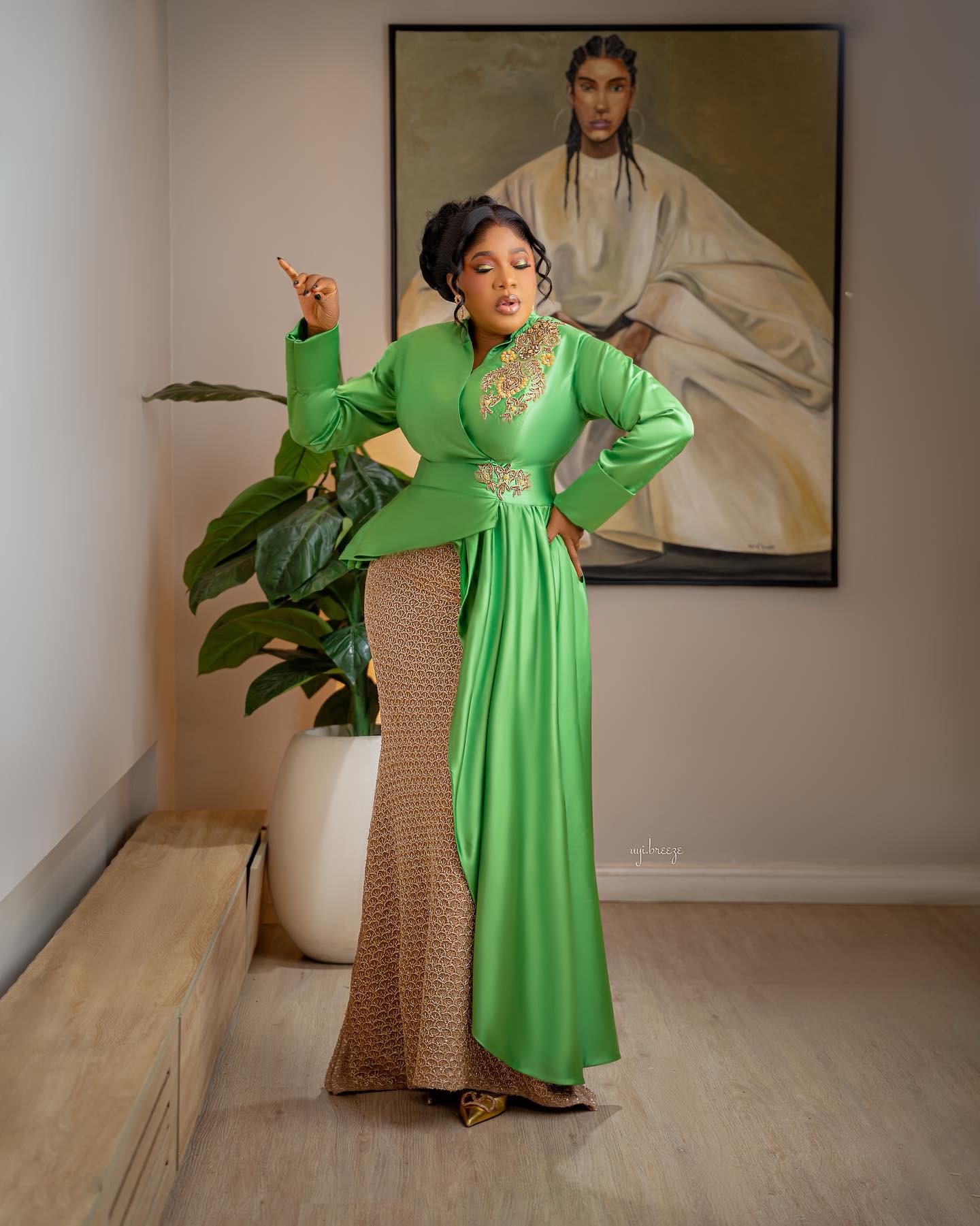 Toyin Abraham Ajeyemi with a fluid apple-green satin panel cascading from the waist over a fitted floor-length gold column skirt.